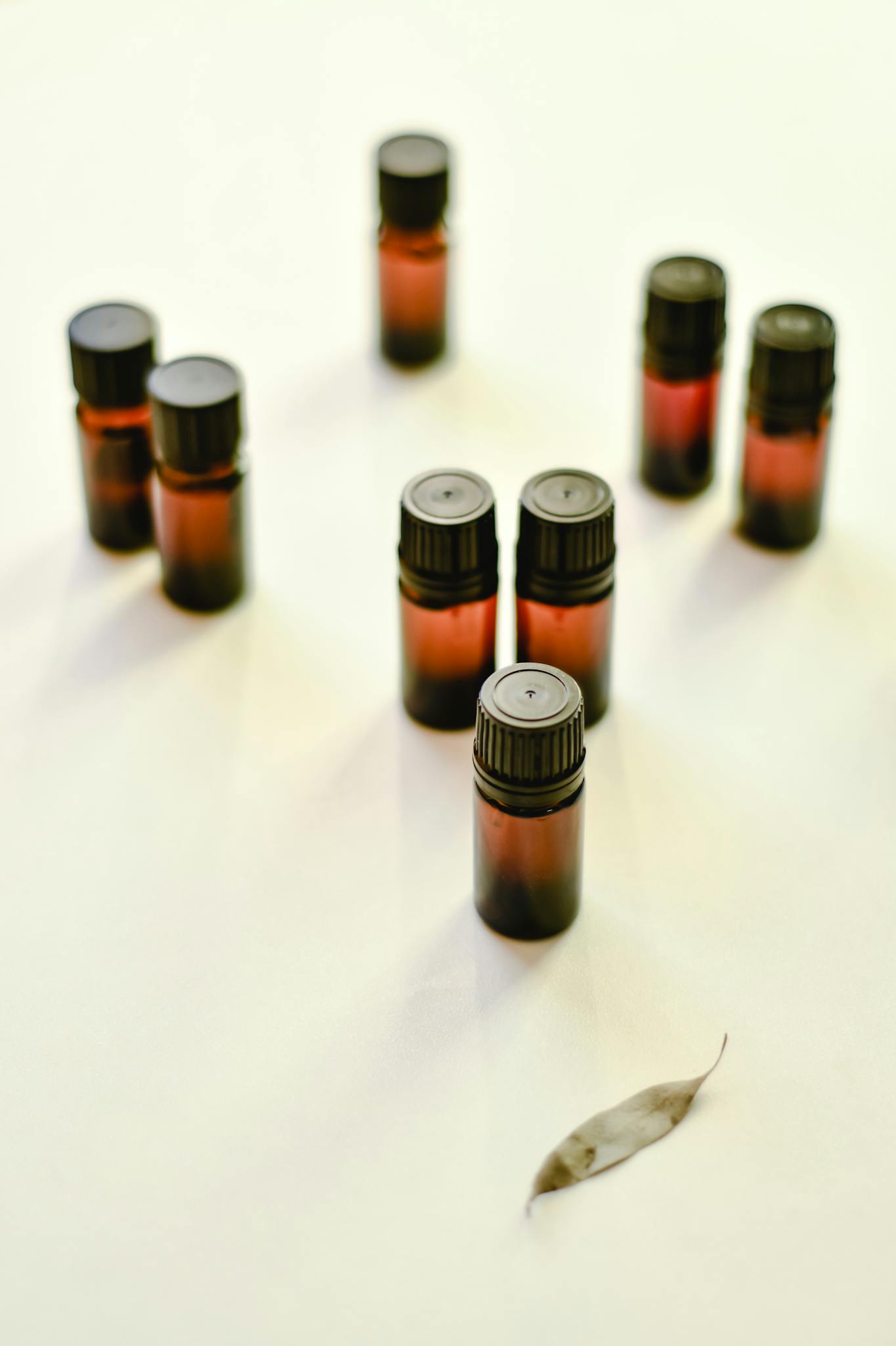 Eight amber essential oil bottles arranged on a white surface with a single leaf.